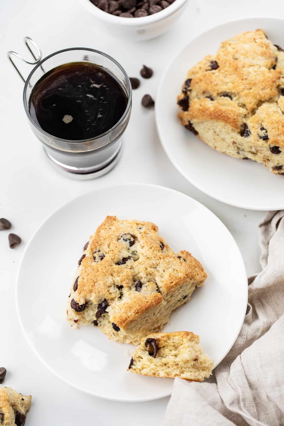Chocolate Chip Scones on white plates next to coffee on a white counter top.