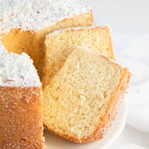Slices of Coconut Chiffon Cake on a cake stand stacked against the cake.