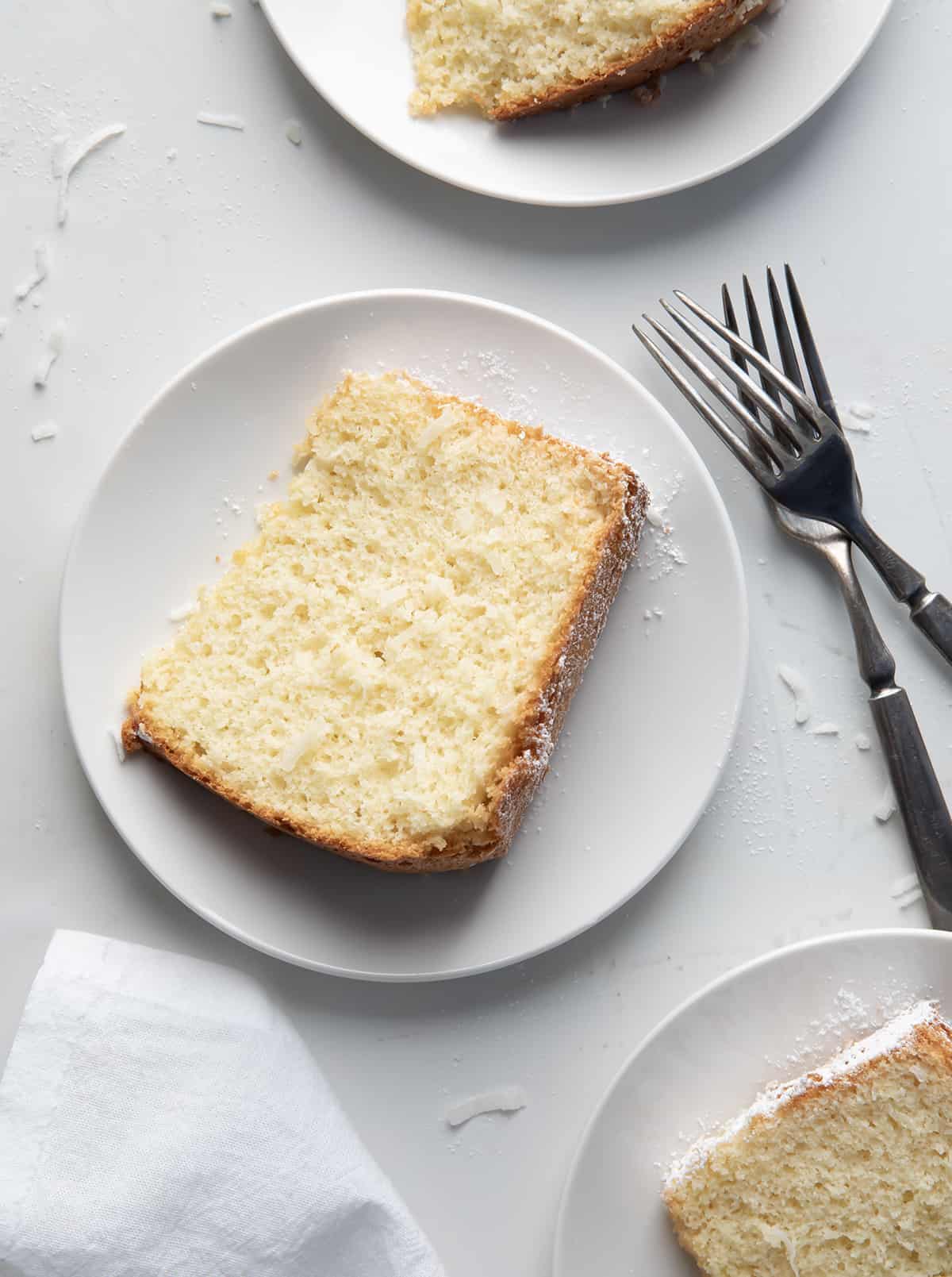 Slices of Coconut Chiffon Cake on white plates on a white table from overhead.