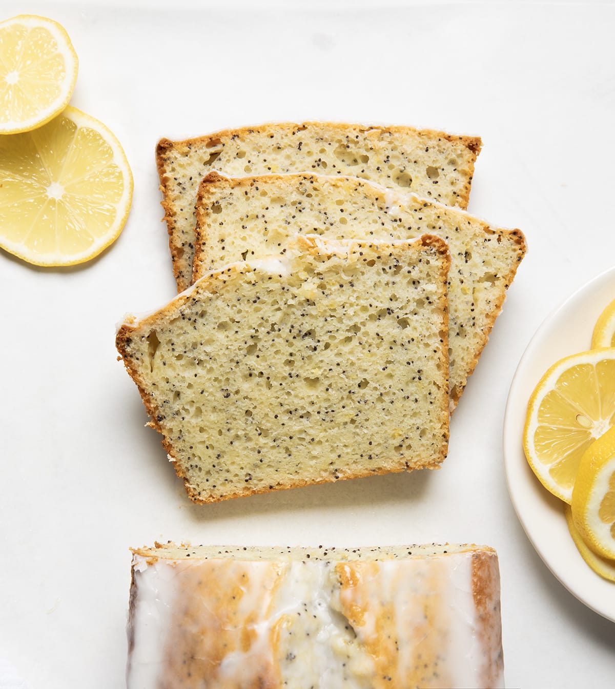 Slices of Lemon Poppy Seed Bread laying flat on a white table next to the loaf from overhead.