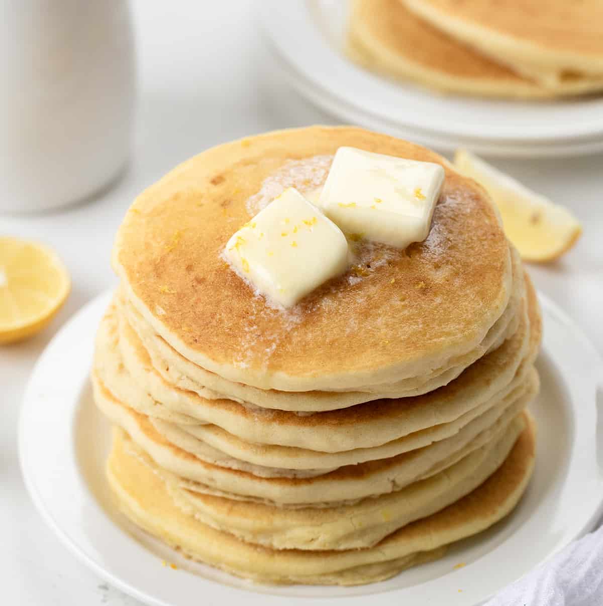 Stack of Lemon Ricotta Pancakes with melting butter and more pancakes in the background.