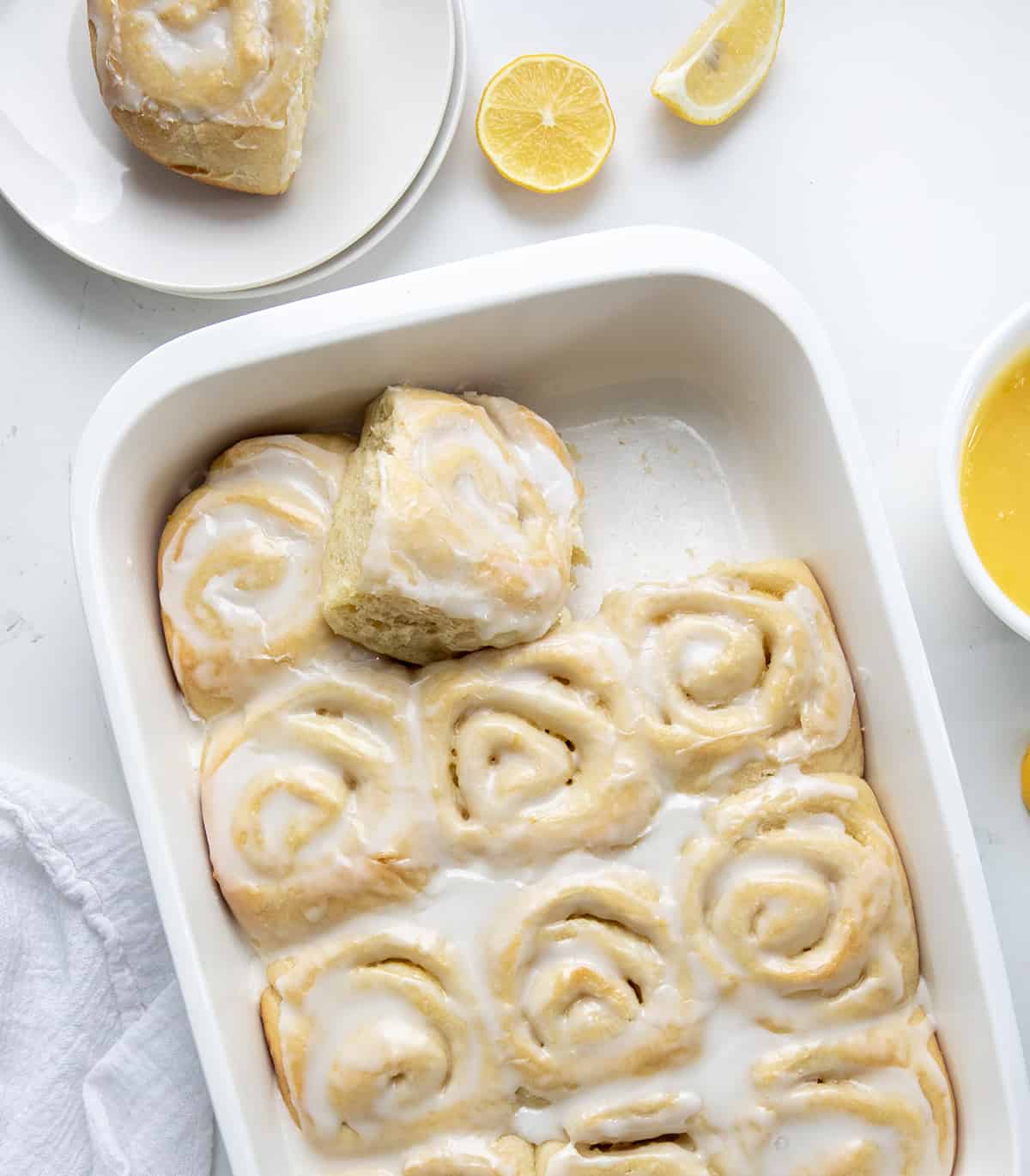 Pan of Lemon Sweet Rolls on a white table with one roll removed. 
