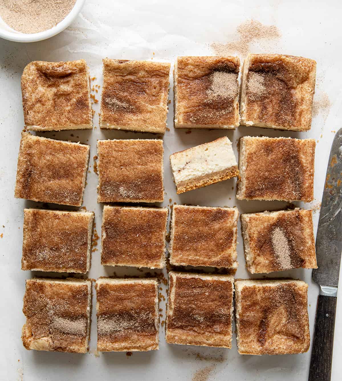 Snickerdoodle Cheesecake Bars cut into squares and one bar flipped on it's side. 