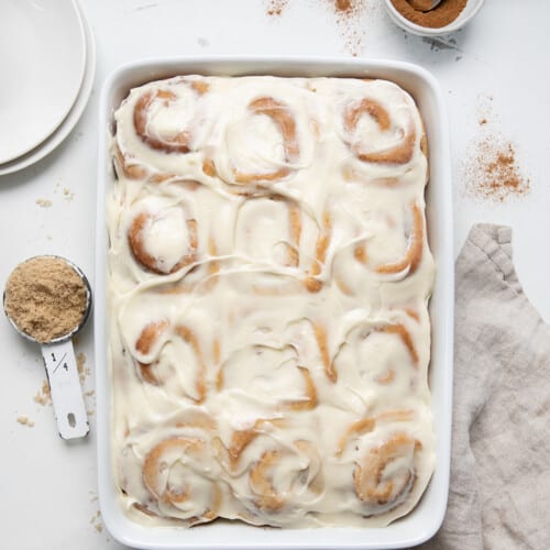 Pan of Amish Cinnamon Rolls (or Potato Cinnamon Rolls) on a white counter with a towel and plates near it from overhead.