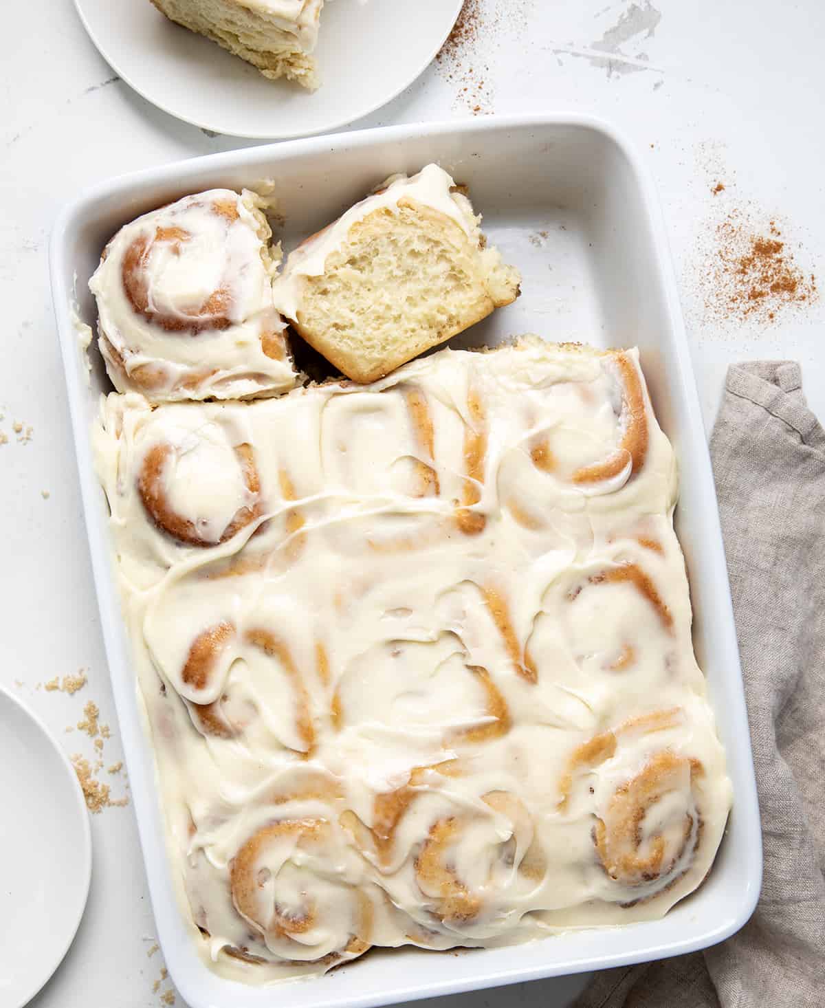 Pan of Amish Cinnamon Rolls (or Potato Cinnamon Rolls) on a white counter with one roll removed and one roll on its side.