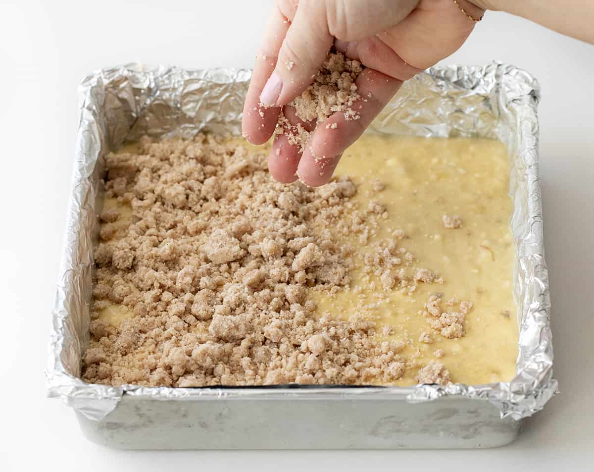 Adding the crumb to a banana crumb cake batter in a foil lined pan.