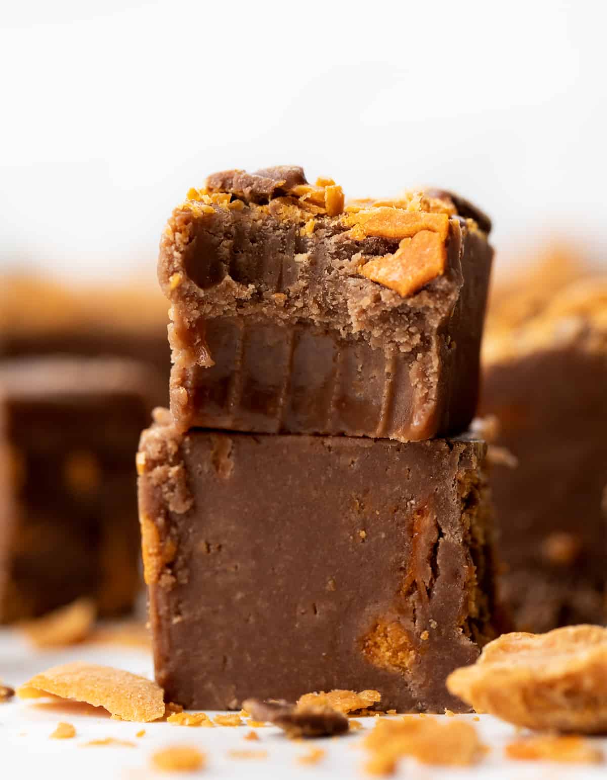 Pieces of Butterfinger Fudge on a white counter with top piece bit into showing creamy texture of fudge.