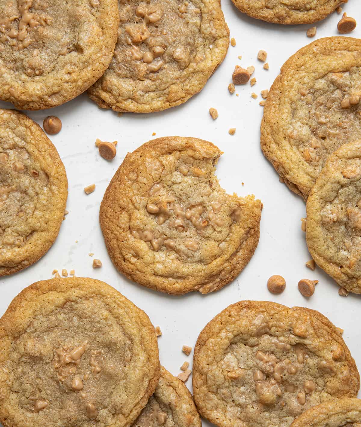 Butterscotch Toffee Cookies on a white table with center cookie having a bite taken out of it.