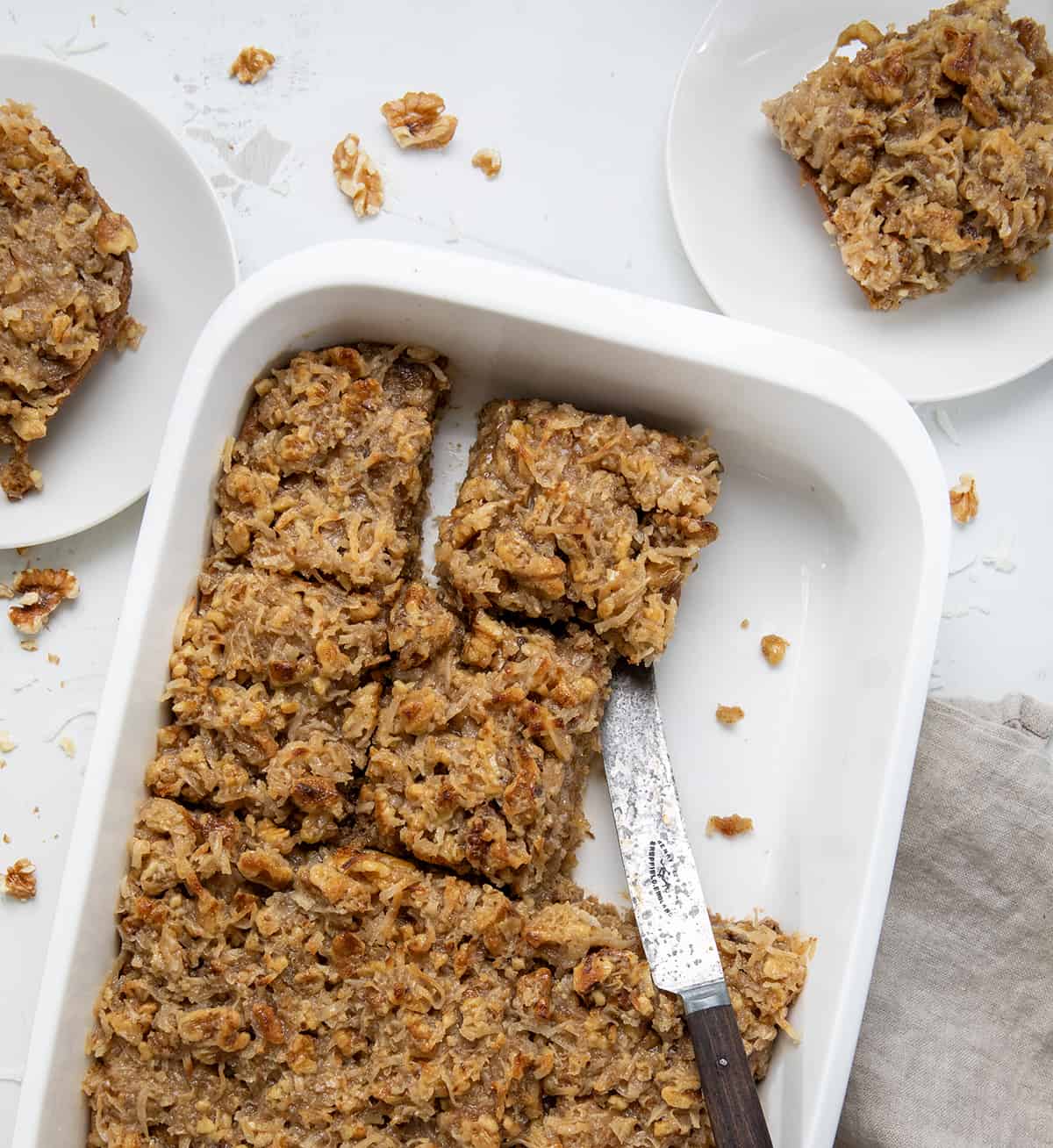 Pan of Old Fashioned Oatmeal Cake with pieces cut up and a knife in the pan from overhead. 