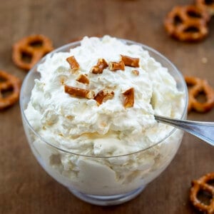 Bowl filled with Pineapple Pretzel Fluff with broken pretzels on top and surrounded by whole pretzels.