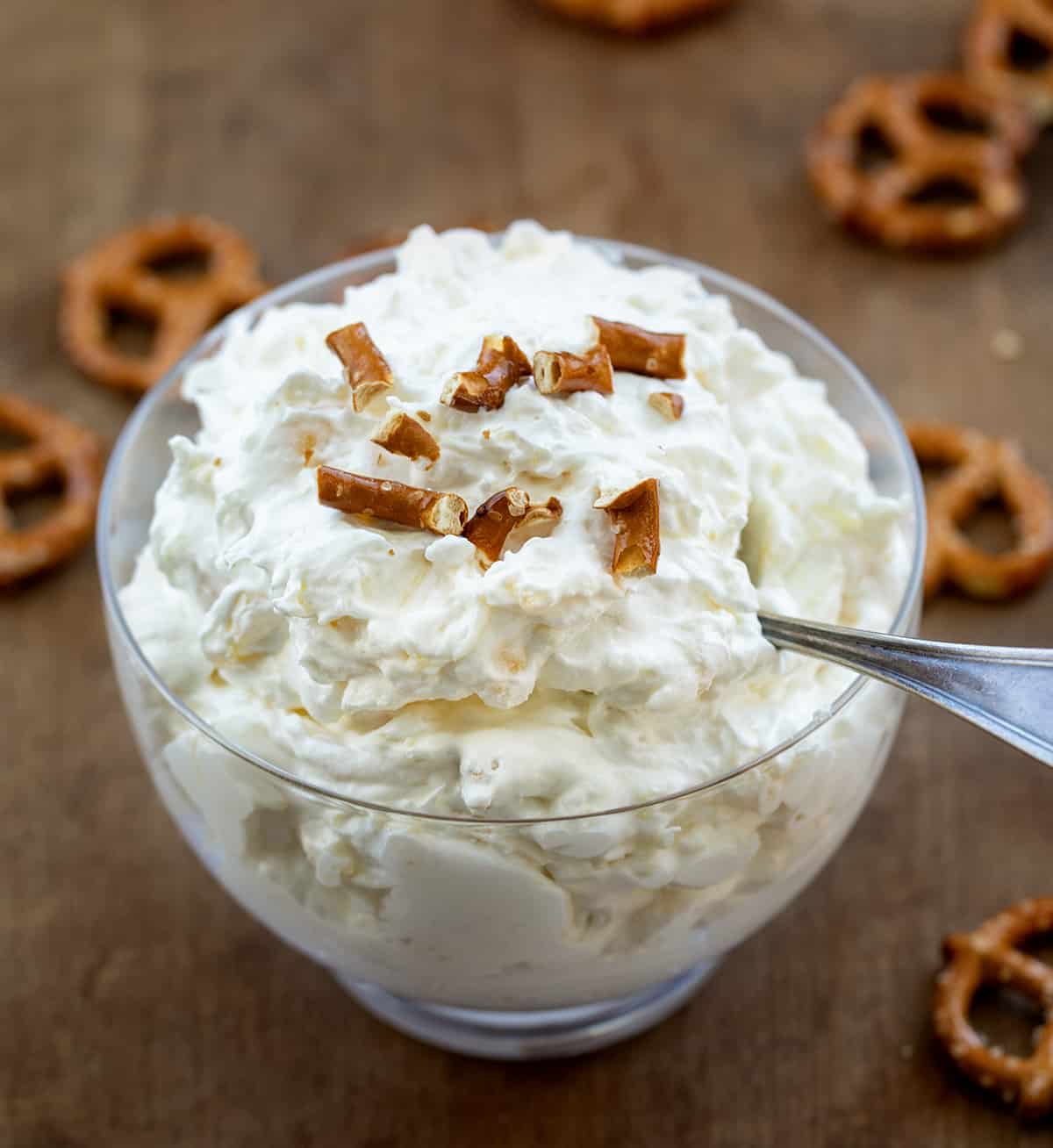 Bowl filled with Pineapple Pretzel Fluff with broken pretzels on top and surrounded by whole pretzels.