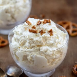 Bowl filled with Pineapple Pretzel Fluff with broken pretzels on top and surrounded by whole pretzels.