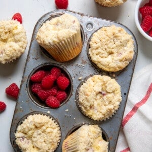 Raspberry Muffins in a pan on a white counter with raspberries.