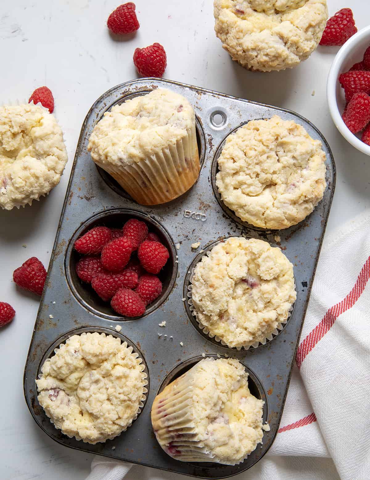Raspberry Muffins in a pan on a white counter with raspberries.