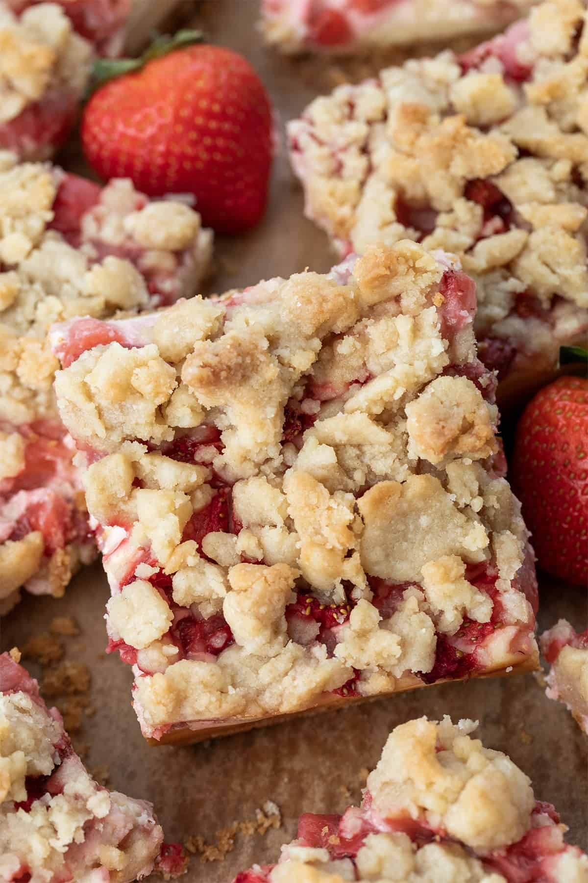 Close up of Strawberry Cheesecake Bars clustered together on a counter with strawberries.