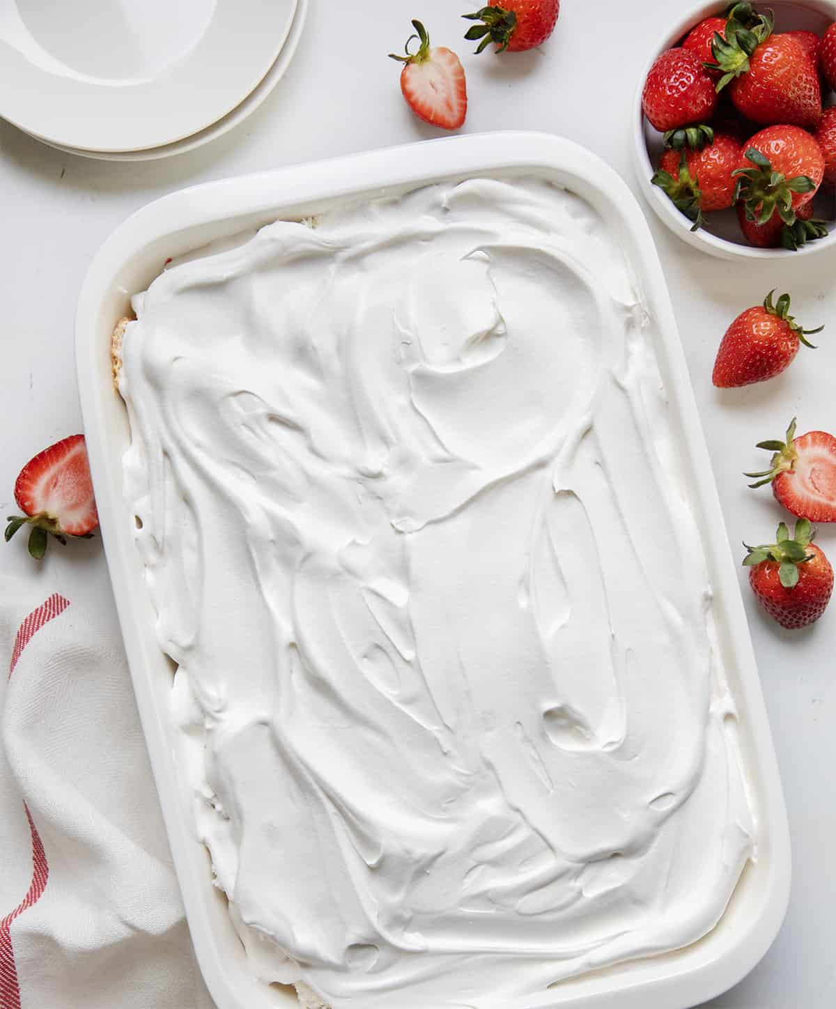 Pan of Strawberry Heaven Dessert covered in whipped cream on a white counter with strawberries around it.