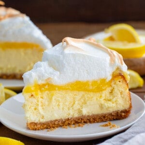 Slice of Lemon Meringue Cheesecake on a white plate on a wooden table.