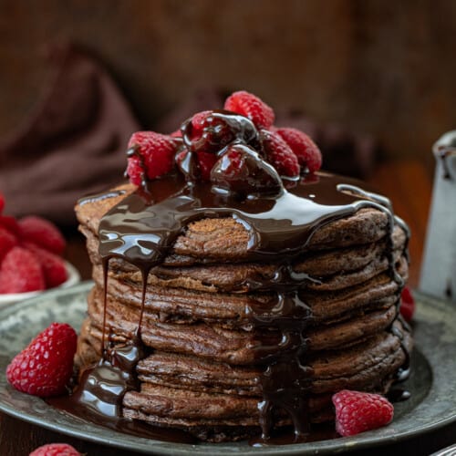 Stack of Chocolate Pancakes with chocolate drizzled over top.