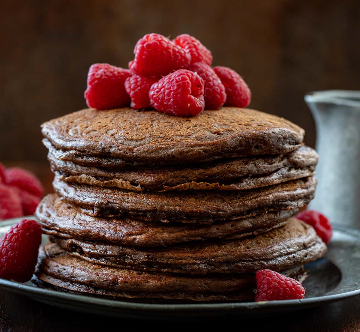 Stack of Chocolate Pancakes with raspberries on top on a wooden table. 