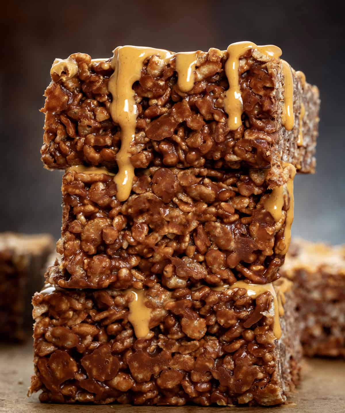 Stack of Chocolate Peanut Butter Rice Krispie Bars on a wooden table surrounded by other bars.