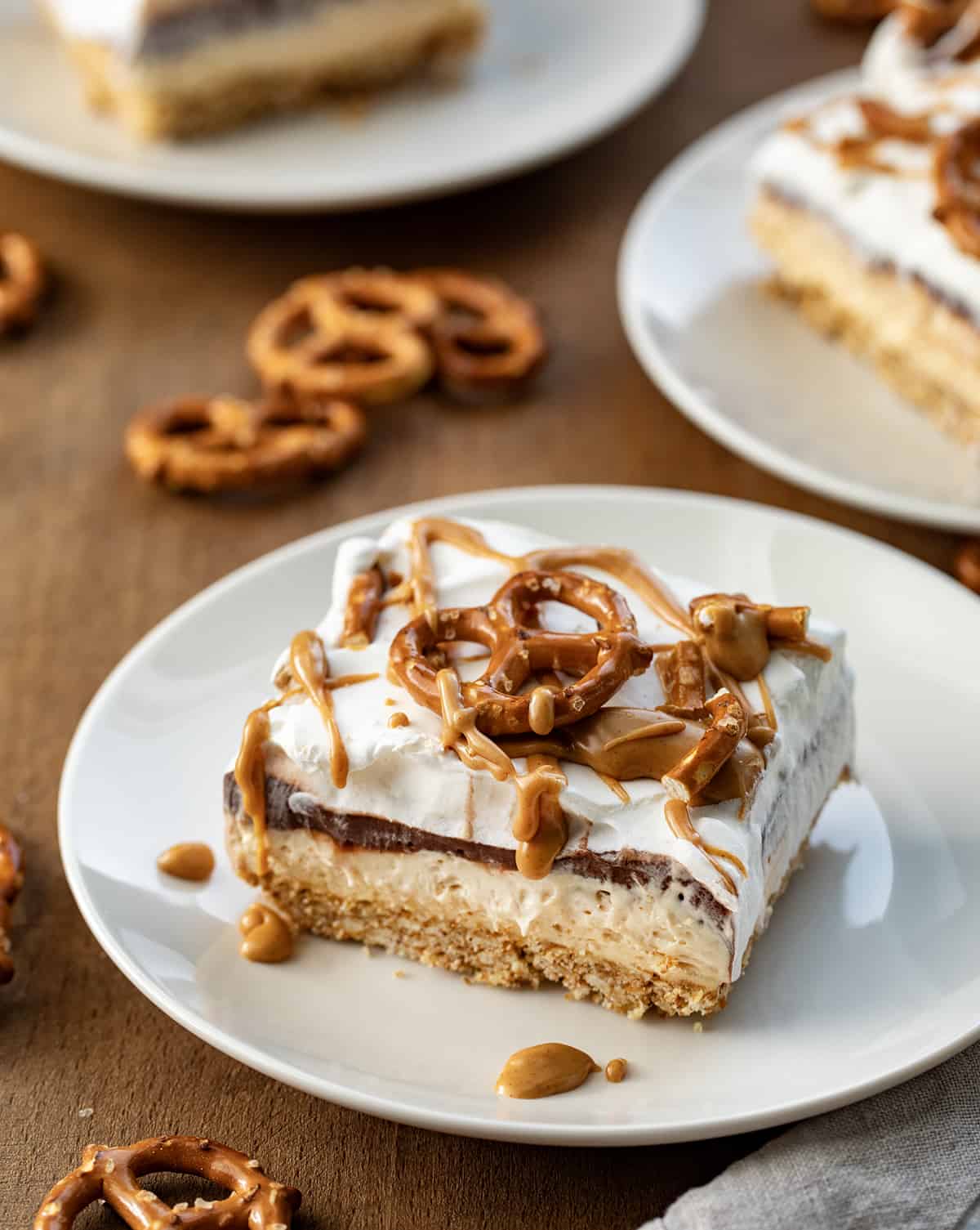 Pieces of Peanut Butter Pretzel Dessert on white plates on wooden table.