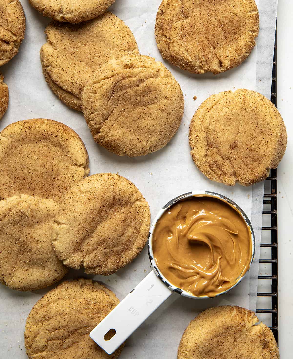 Peanut Butter Snickerdoodles on a cooling rack with a measuring cup of peanut butter. 