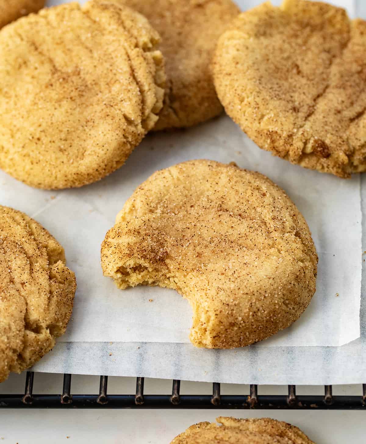 Peanut Butter Snickerdoodles cooling on a rack and one with a bite take out of it.