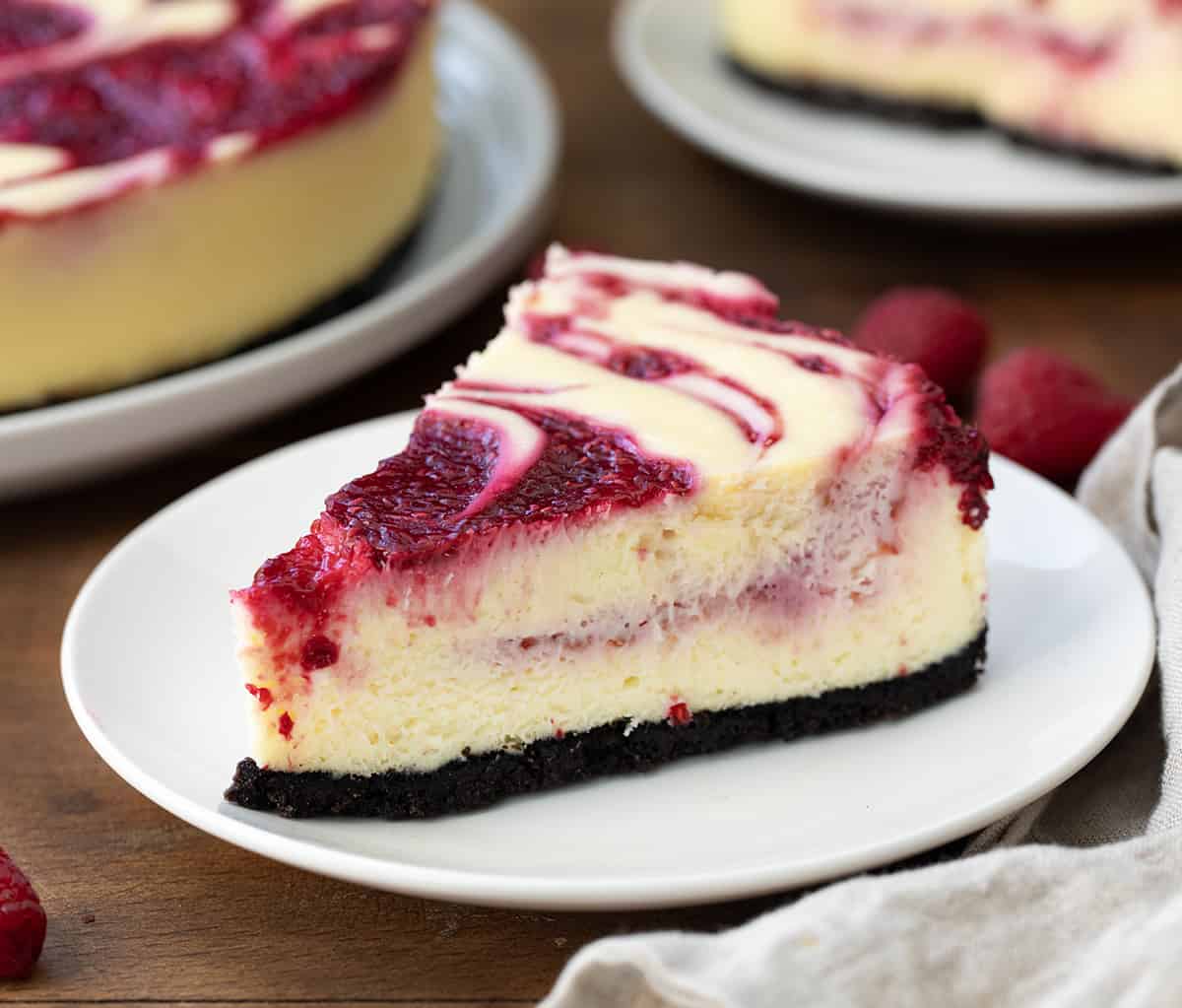 Piece of White Chocolate Raspberry Cheesecake on a white plate on a wooden table.
