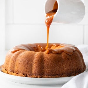 Pouring caramel over Salted Caramel Pound Cake on a white counter.