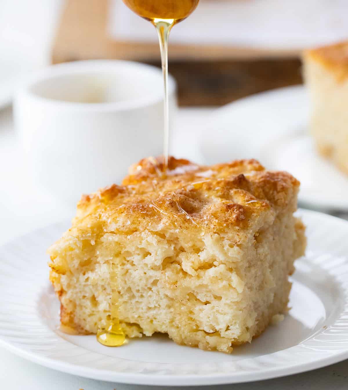 Drizzling honey over a Cinnamon Honey Butter Swim Biscuit on a plate.