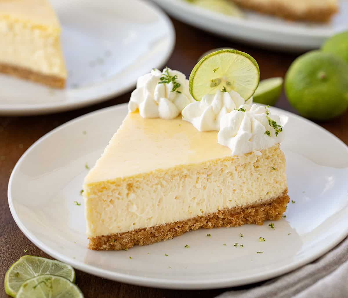 A piece of Key Lime Cheesecake on a white plate on a wooden table.