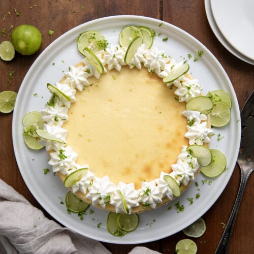 Key Lime Cheesecake on a white serving platter on a wooden table from overhead.