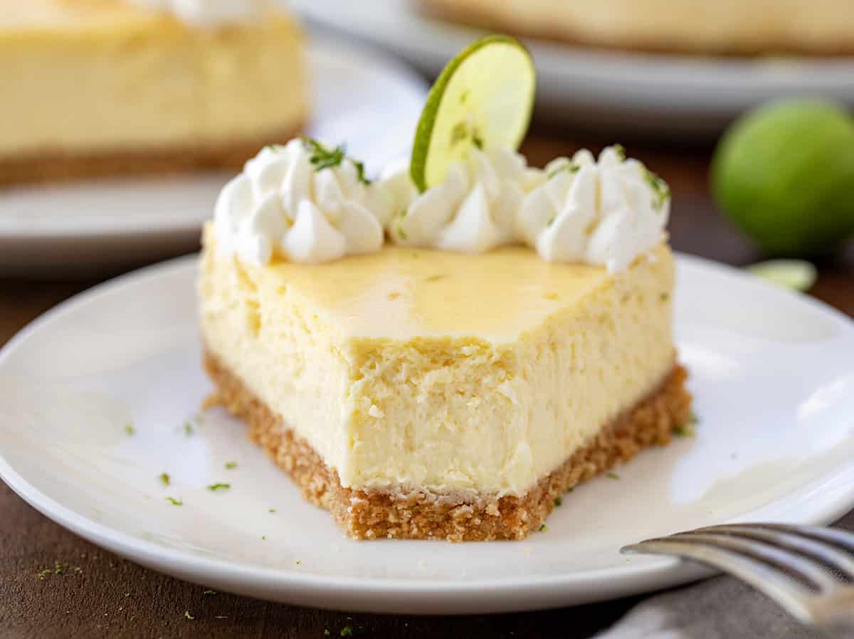 A piece of Key Lime Cheesecake on a white plate on a wooden table with a bite removed.