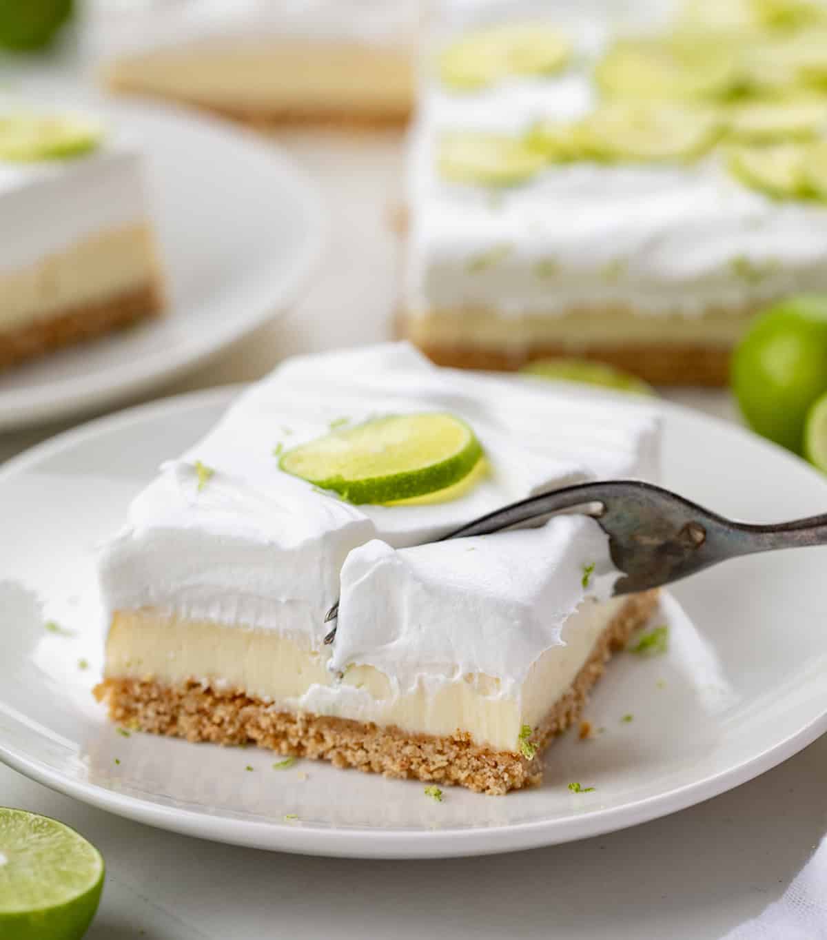 One Key Lime Pie Bar on a white plate with a fork taking a bite.