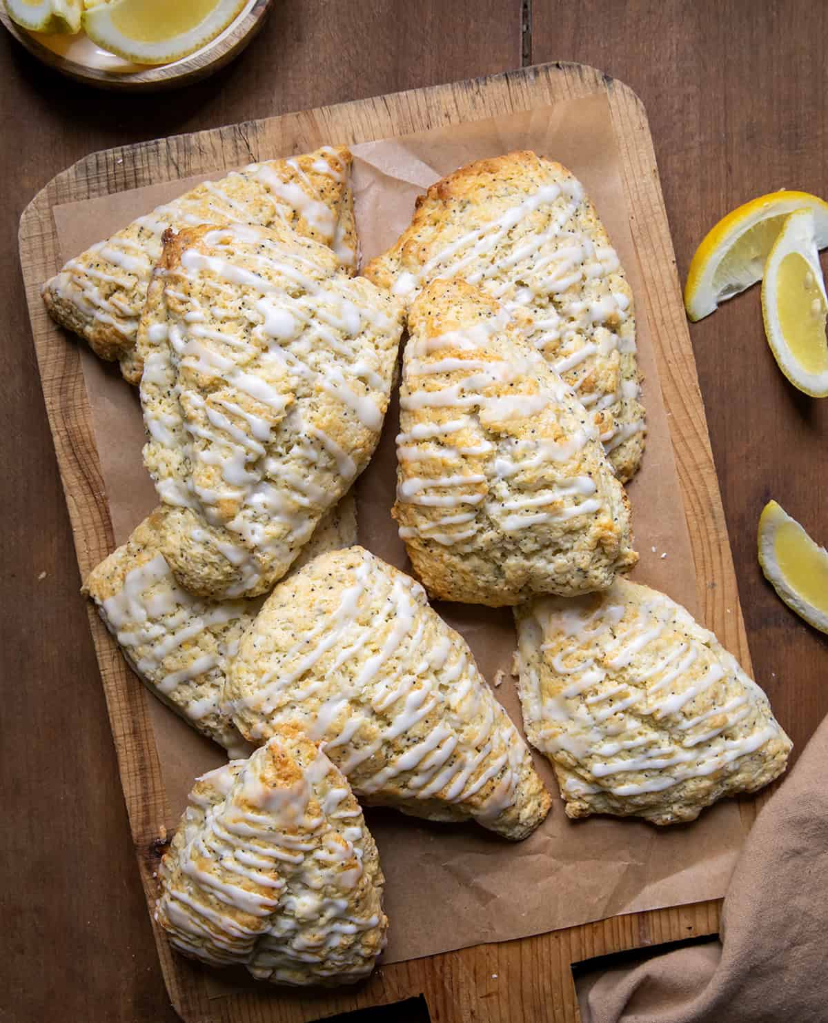 Lemon Poppy Seed Scones on a wooden cutting board on a table surrounded by lemon slices from overhead.