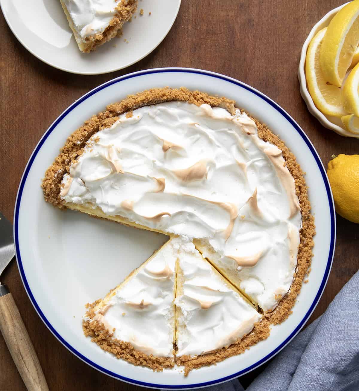 Magic Lemon Pie in a pie dish with some pieces cut and one piece on a white plate from overhead. 