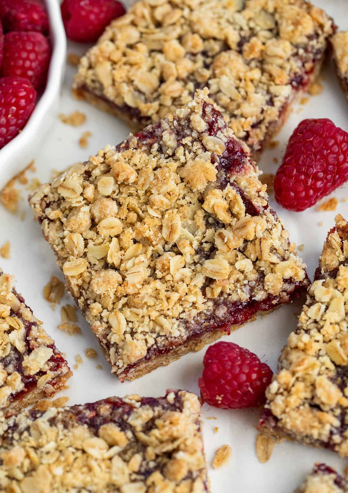 Scattered Raspberry Oatmeal Crumble Bars on a white table.