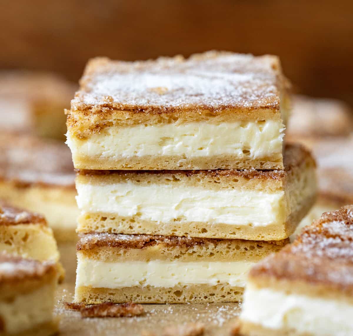 Stack of Churro Cheesecake Bars on a wooden table with more bars surrounding the stack.