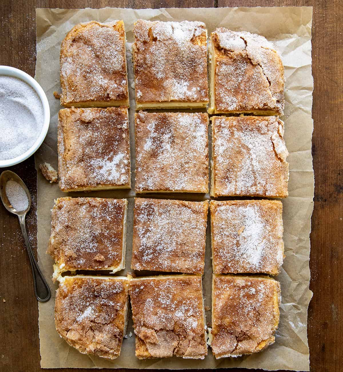 Churro Cheesecake Bars cut into pieces on a piece of parchment paper on a wooden table from overhead. 