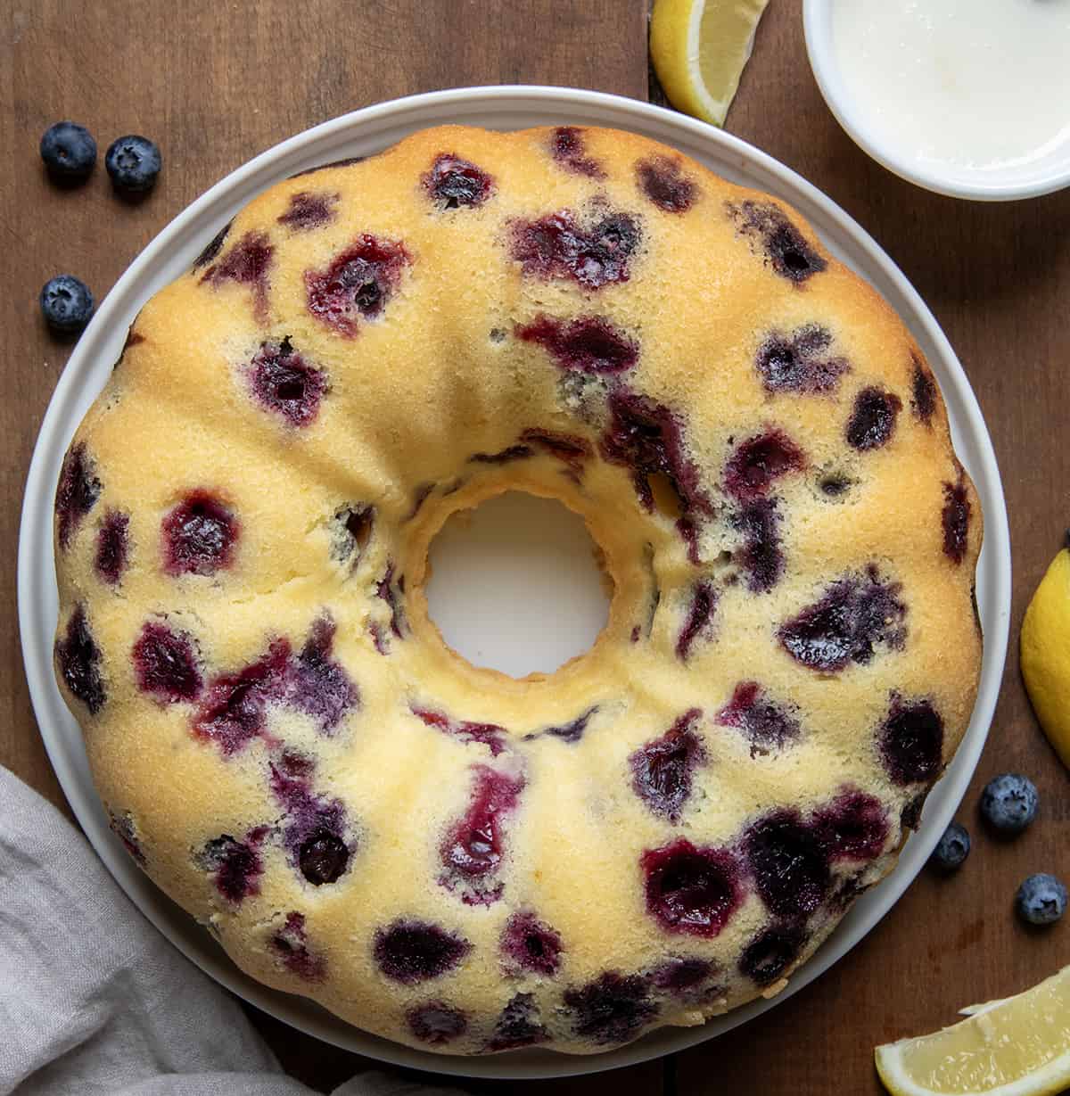 Lemon Blueberry Pound Cake on a cake plate before glazing, with a bowl of glaze off to the side.