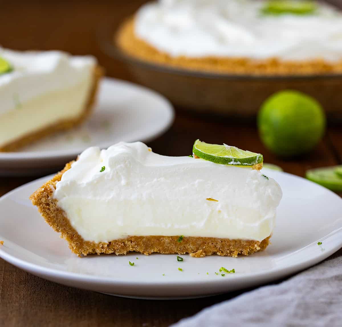Pieces of key lime pie on white plates on a dark wooden table.