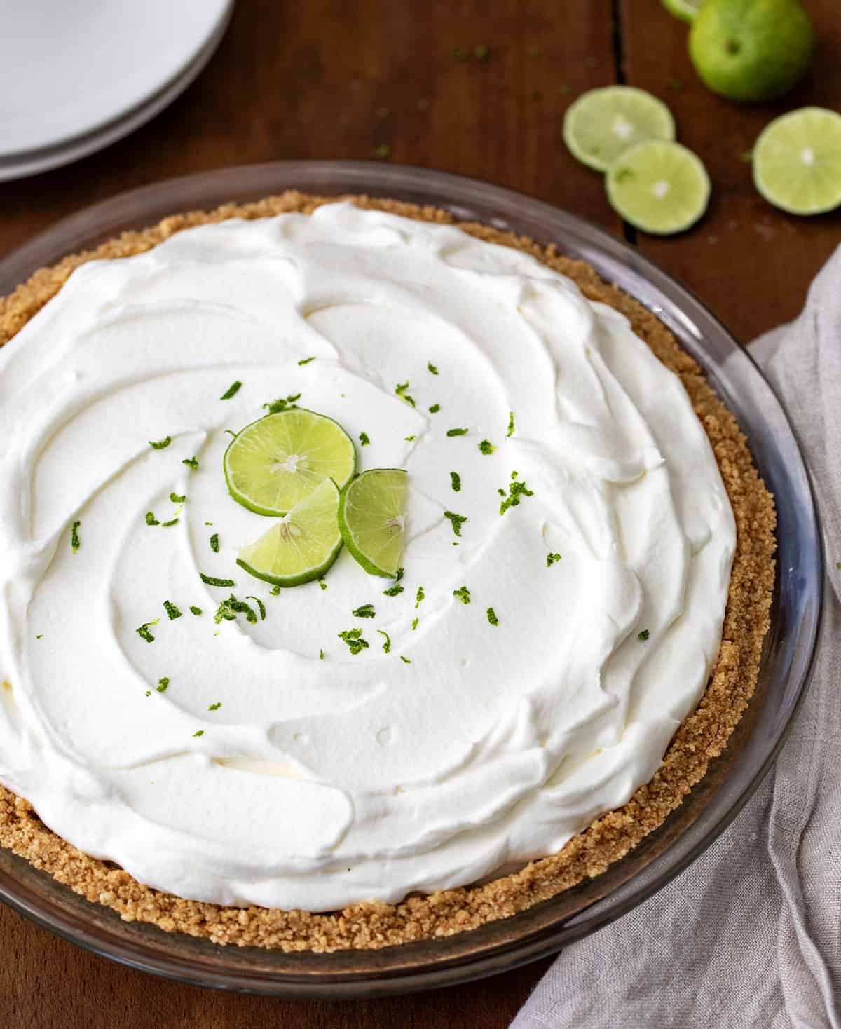 Whole No Bake Key Lime Pie on a wooden table with fresh key limes garnish on top.