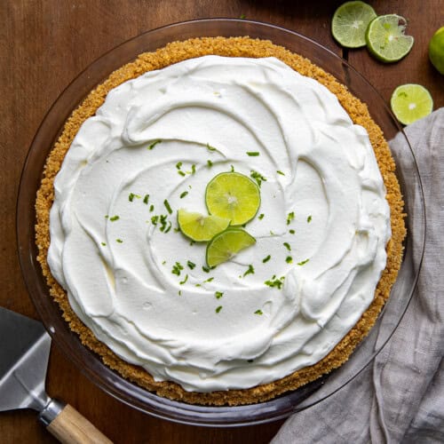 Whole No Bake Key Lime Pie on a wooden table with fresh key limes from overhead.