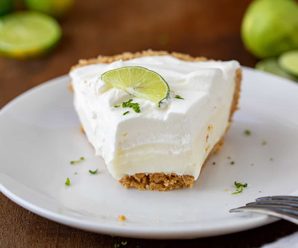 Piece of key lime pie on a white plate with a bite removed and fork resting on the side of the plate.
