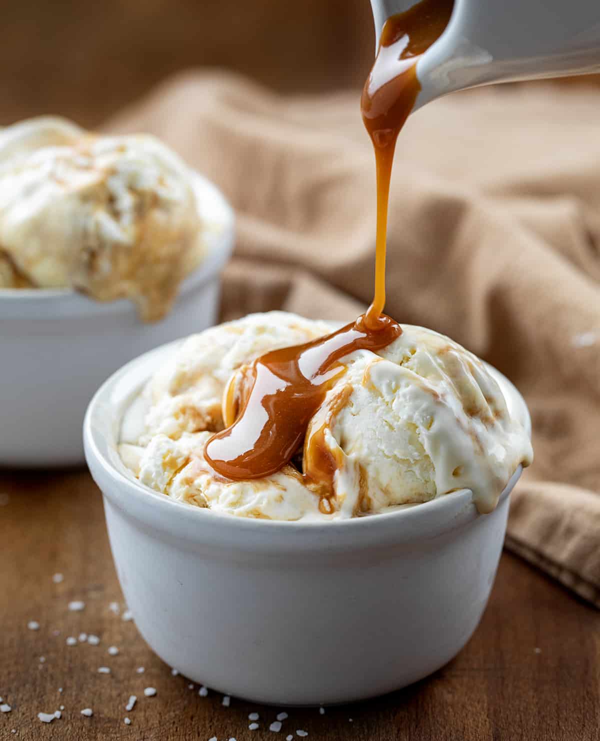 Pouring caramel over bowl of homemade No Churn Salted Caramel Ice Cream on a wooden table.