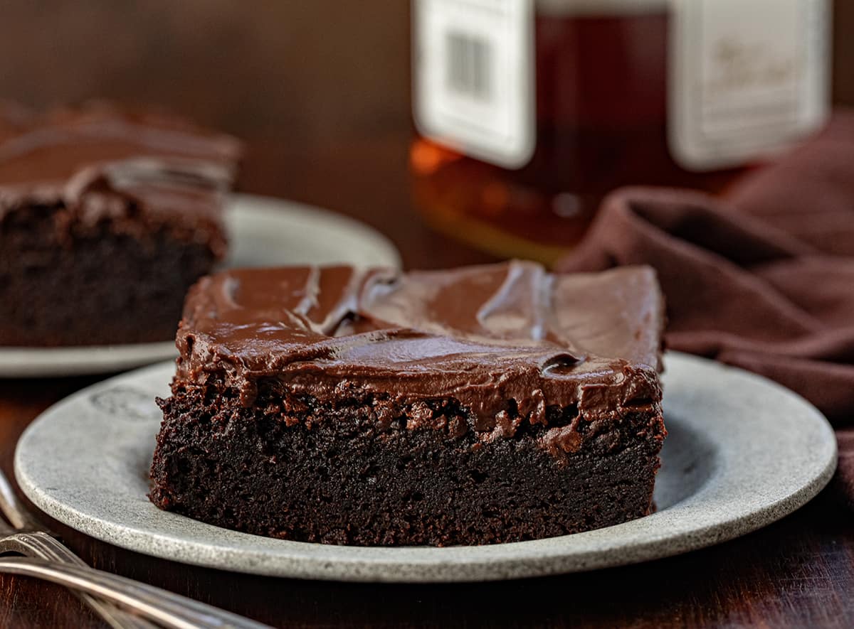 Piece of Double Fudge Whiskey Cake on a plate with a bottle of whiskey in the background.
