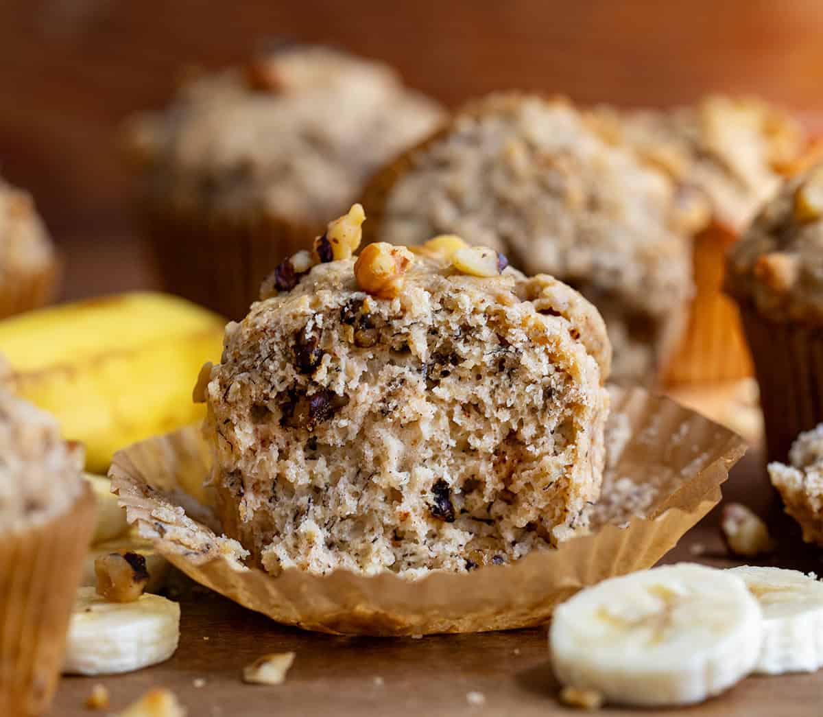 Banana Nut Muffins on a wooden table with the center muffin cut in half showing inside texture.