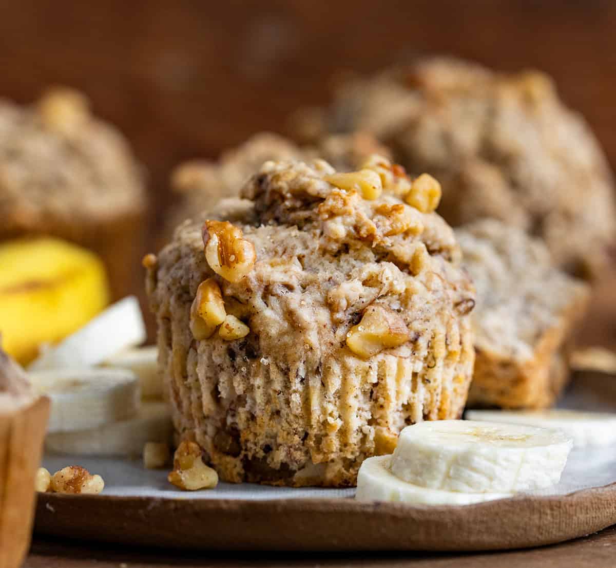 Banana Nut Muffins on a wooden table with bananas and banana slices.