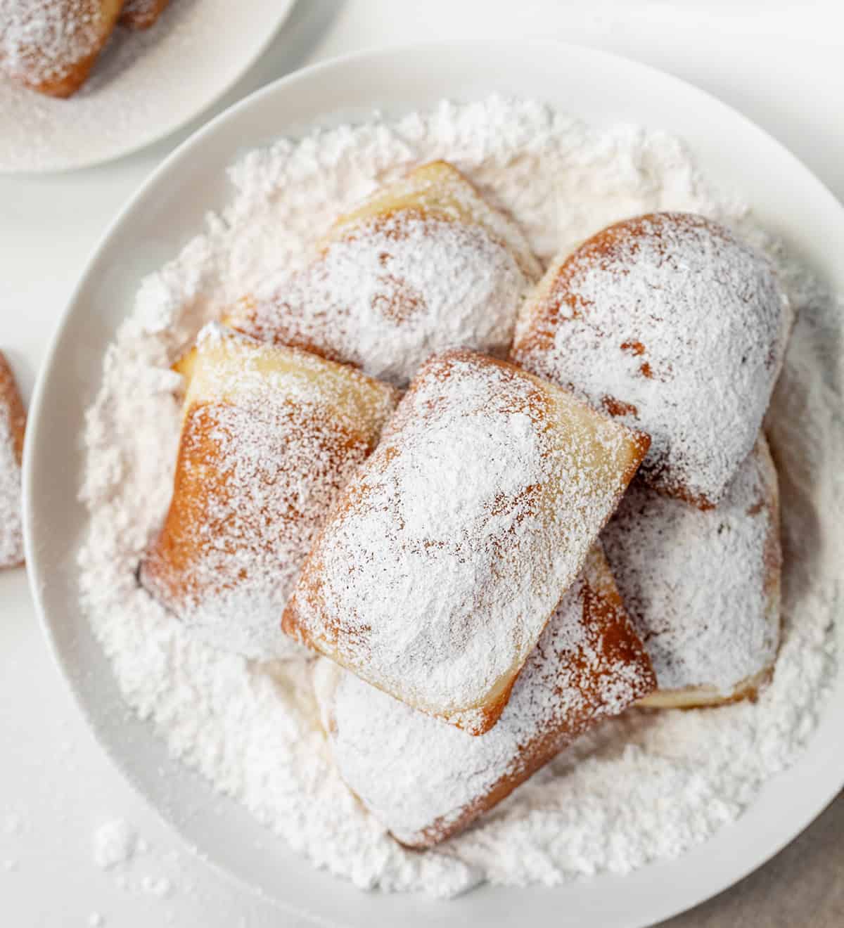 Plate of Beignets surrounded by confectioners sugar on a white counter.