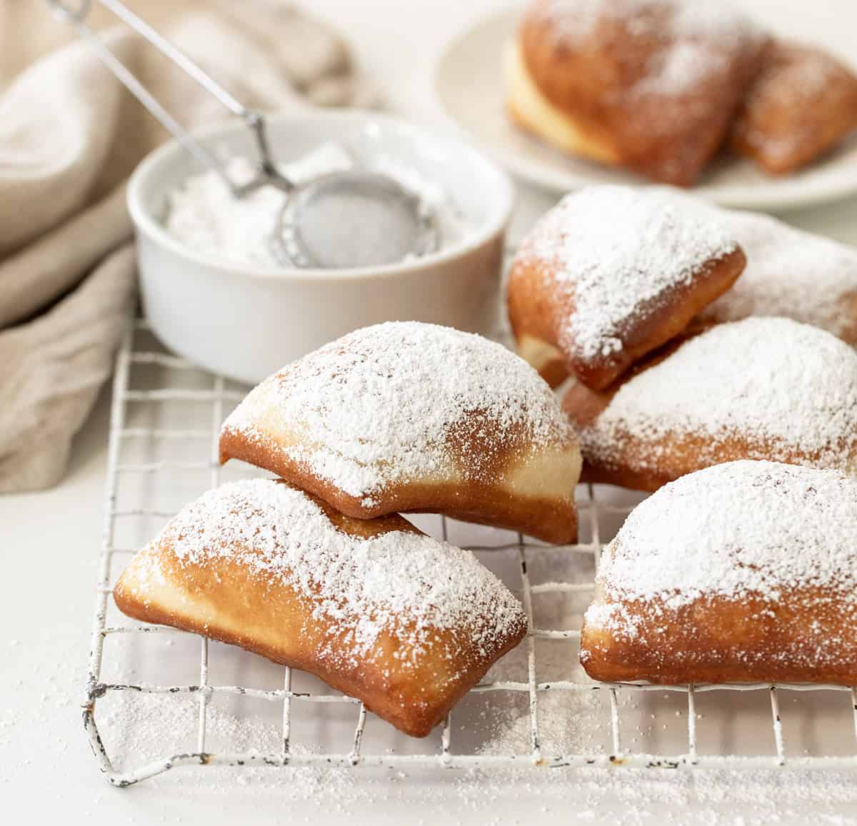 Beignets on a cooling rack dusted in powdered sugar. 